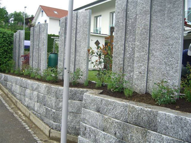 Stelen auf Mauersteinen versetzt. Phantasievolle Gartenabgrenzung.